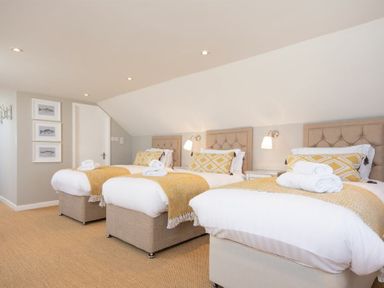 A bedroom with three single beds with yellow throw blankets and pillows at Cargoes in Craster