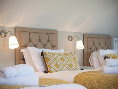 A bedroom with two beige headboards two beds white linens yellow patterned cushions and wall lights at Cargoes in Craster