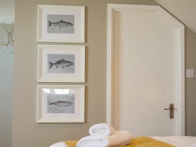 A wall with three framed fish prints next to a white door with a silver handle and a bed with folded white towels and a yellow blanket at Cargoes Craster
