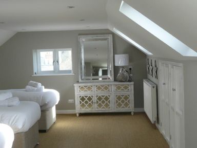 A bedroom with two beds and rolled towels near a window a decorative cabinet with a mirror and a lamp on it at Cargoes in Craster