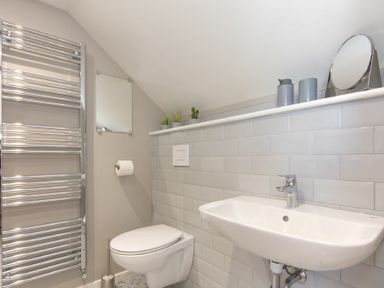 A bathroom with a wall-mounted toilet a white sink a chrome towel radiator and small plants on a shelf at Cargoes in Craster