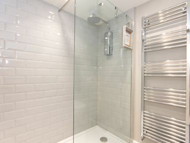A shower area with glass door white subway tiles and a chrome towel radiator at Cargoes Craster