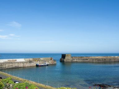 A harbor with stone piers and a small boat in the water at Cargoes in Craster