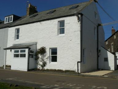 A white stone house with several windows a chimney and a small porch at Cargoes in Craster