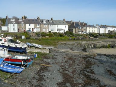A shoreline with boats on rocky beach and a row of houses in the background at Cargoes in Craster
