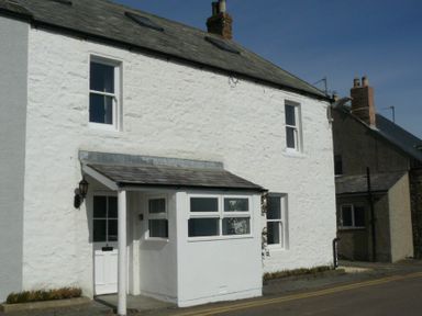 Exterior of a two-story white stone house with a small porch on a street at Cargoes in Craster