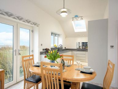 A dining area with a wooden table set for four and a kitchen with white cabinets and a skylight at Viewpoint in Alnmouth