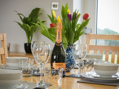 A dining table set with bowls plates wine glasses and a bottle of prosecco with a vase of tulips at Viewpoint in Alnmouth