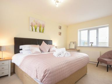 A bedroom with a bed with pink bedding bedside tables and a window at Viewpoint in Alnmouth
