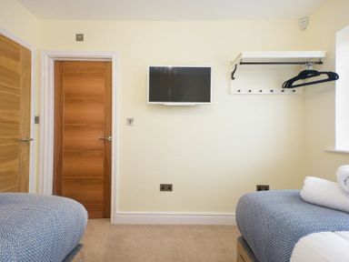 A bedroom with two beds a wall-mounted television wooden doors and a wall rack with hangers at Viewpoint in Alnmouth