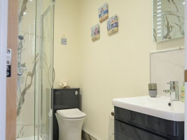 A bathroom with a shower enclosure a toilet a sink with a cabinet and wall decorations at Viewpoint in Alnmouth