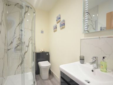 A bathroom with a glass shower enclosure a toilet and a sink with a mirror at Viewpoint in Alnmouth