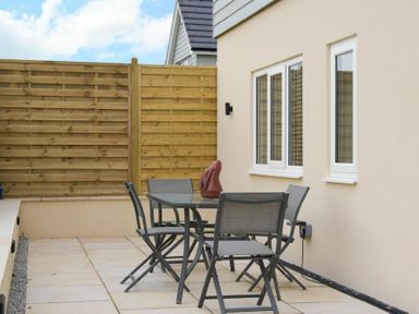 A patio area with a glass table and four chairs next to a house with three windows and a wooden fence at Viewpoint in Alnmouth
