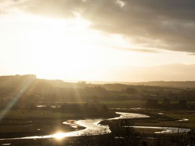 A river winding through fields with hills and trees under a cloudy sky at Viewpoint in Alnmouth