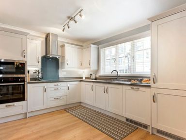 A kitchen with white cabinets stainless steel appliances a window with blinds and a striped rug on the floor at Castlewood in Bamburgh
