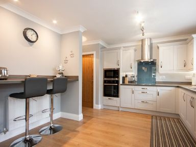 A kitchen with two bar stools at a counter and cabinets with appliances at Castlewood in Bamburgh