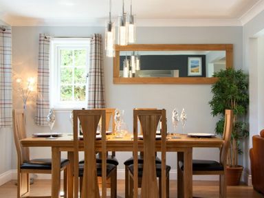 A dining room with a wooden table and six chairs set with glassware and plates at Castlewood in Bamburgh