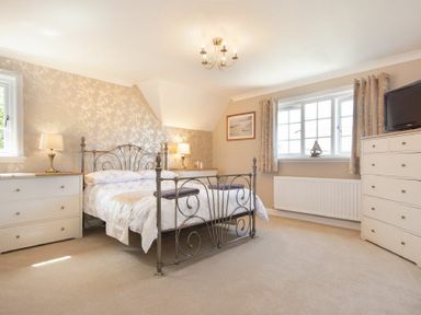 A bedroom with a metal bed frame two dressers a window with curtains and a television at Castlewood in Bamburgh
