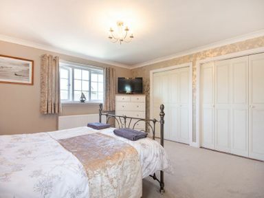 A bedroom with a bed a window with curtains a chest of drawers and built in wardrobes at Castlewood in Bamburgh
