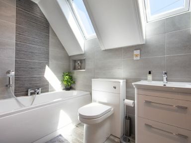 A bathroom with a bathtub a toilet a sink and skylight windows at Castlewood Bamburgh