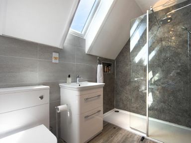 A bathroom with a toilet sink vanity and walk in shower under skylight windows at Castlewood in Bamburgh