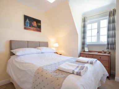 A bedroom with a double bed bedside lamp and chest of drawers under a window at Castlewood in Bamburgh