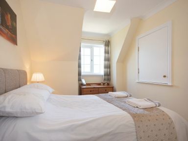 A bedroom with a bed, bedside lamp, chest of drawers, window with curtains at Castlewood in Bamburgh