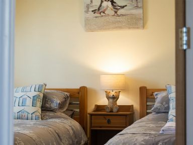 A bedroom with two single beds a wooden nightstand and a lamp shaped like a dog at Castlewood in Bamburgh