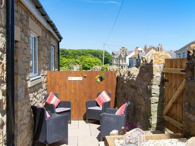 An outdoor patio area with four chairs with cushions and a wooden gate surrounded by stone walls at Castlewood in Bamburgh