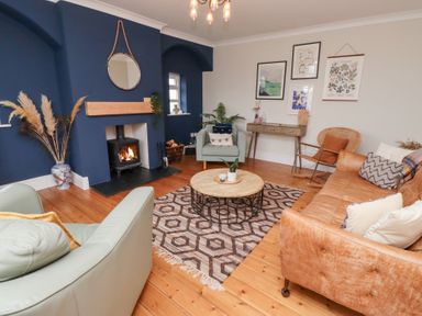 A living room with a fireplace blue accent wall armchairs a leather sofa round coffee table and wall art at Rosedale Lodge in Alnmouth