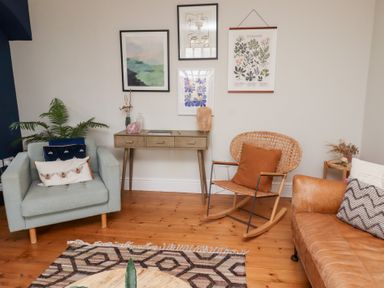A room with a light blue armchair and a brown leather sofa next to a wooden rocking chair and console table with framed artwork on the wall at Rosedale Lodge in Alnmouth