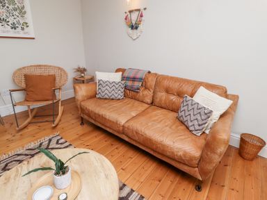 A living room with a brown leather sofa and cushions a wooden rocking chair with a cushion a round wooden coffee table with a plant and dish on it at Rosedale Lodge in Alnmouth