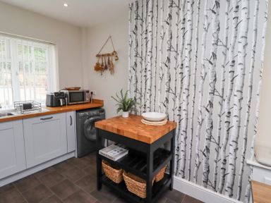 A kitchen corner with grey cabinets wooden countertop a microwave toaster washing machine and a black kitchen island with baskets at Rosedale Lodge in Alnmouth