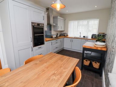 A kitchen with wooden countertops grey cabinets a wooden dining table with chairs and a window with blinds at Rosedale Lodge in Alnmouth