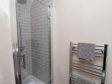 A shower with glass door and tile walls next to a towel rack with towels at Rosedale Lodge in Alnmouth