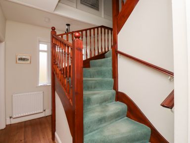 A staircase with green carpet and wooden banister in a hallway at Rosedale Lodge Alnmouth