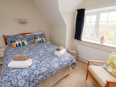 A bedroom with a bed covered in blue floral bedding two nightstands a window with dark curtains and a chair with a cushion at Rosedale Lodge in Alnmouth