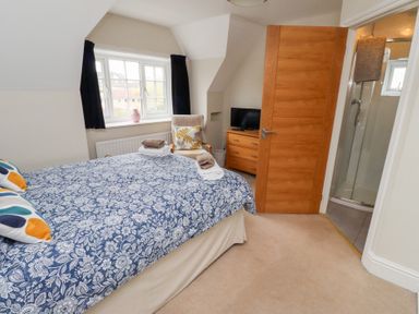 A bedroom with a double bed a wooden door leading to a shower room a wooden chest of drawers with a tv and a window with curtains at Rosedale Lodge in Alnmouth