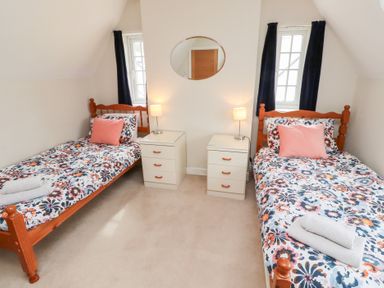 A bedroom with two single beds with floral bedding two nightstands with lamps and an oval mirror on the wall at Rosedale Lodge in Alnmouth
