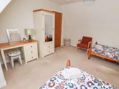 A bedroom with two single beds a wardrobe a desk with a lamp and mirror and an armchair at Rosedale Lodge in Alnmouth