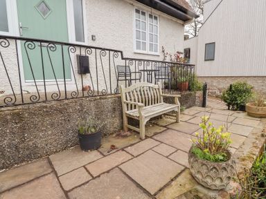 A garden patio with a wooden bench iron railing potted plants and a green door at Rosedale Lodge in Alnmouth