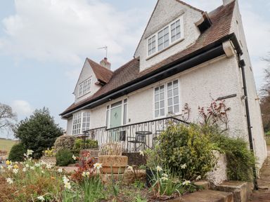An exterior view of a white house with a sloped roof surrounded by plants and flowers at Rosedale Lodge in Alnmouth
