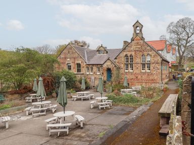 Outdoor seating area with tables and umbrellas in front of a stone building with arched windows at Rosedale Lodge in Alnmouth
