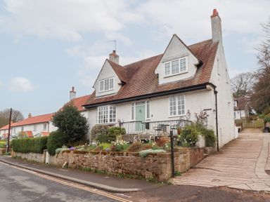A two-story white house with a sloped roof and garden at the front with a driveway to the right at Rosedale Lodge in Alnmouth