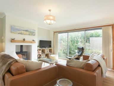 A living room with two brown sofas a glass coffee table a black armchair a television and large sliding glass doors at Spuggies Rest in Embleton