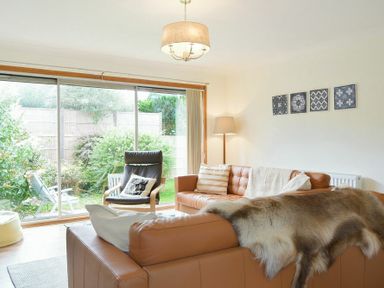 A living room with leather sofas a fur throw a lounge chair and large sliding glass doors overlooking a garden at Spuggies Rest in Embleton