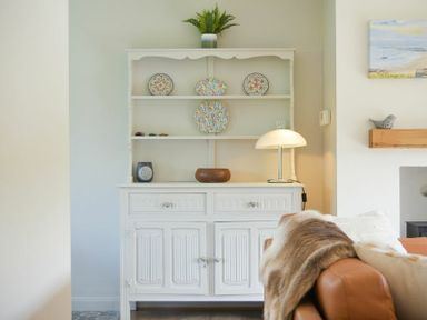 A white wooden cabinet with decorative plates and a lamp next to a brown sofa with a blanket at Spuggies Rest in Embleton