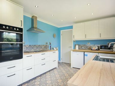A kitchen with white cabinets a stainless steel oven and vent hood a wooden countertop and blue walls at Spuggies Rest in Embleton
