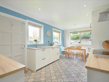 A kitchen with white cabinets wooden countertops a dining table with chairs and blue walls at Spuggies Rest in Embleton