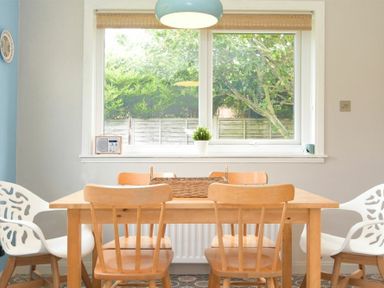 A dining room with a wooden table and chairs near a window with a plant on the sill at Spuggies Rest in Embleton